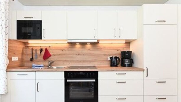 Cocina compacta con gabinetes blancos, horno integrado, microondas y cafetera.