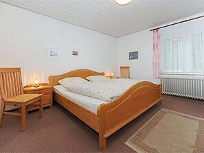 Makuuhuoneessa on puinen sänky, yöpöydät, tuoli, patteri ja ikkuna, jossa on verhot.