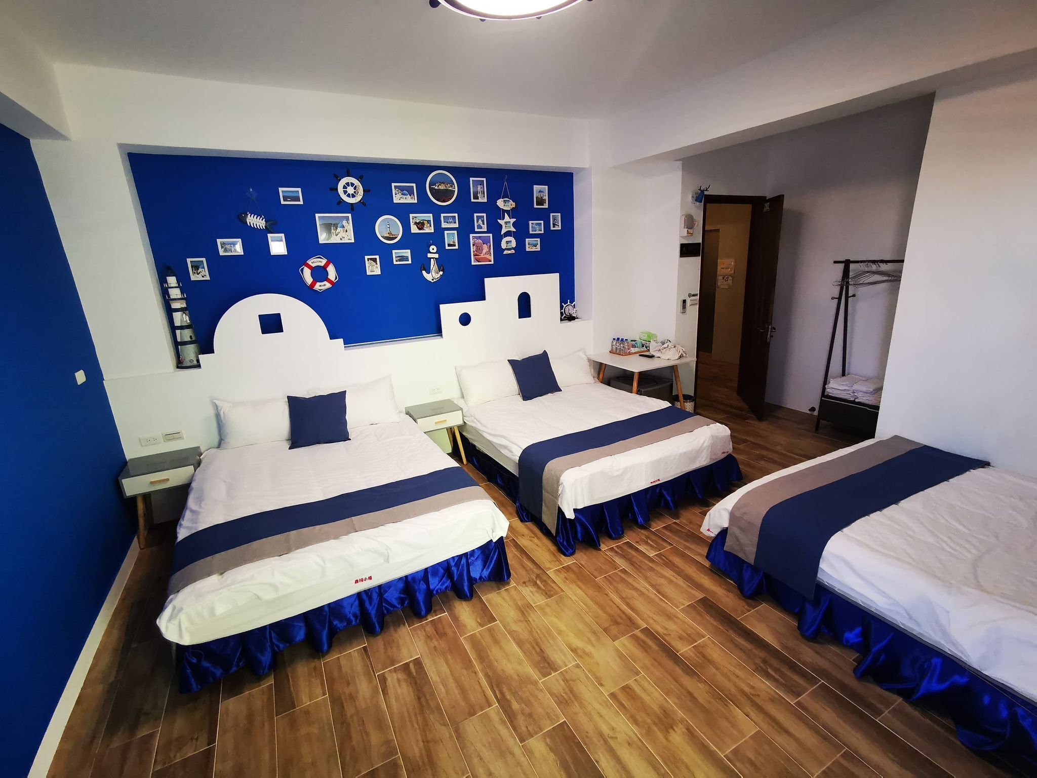 Habitación de hotel con dos camas, una pared azul con fotografías y adornos, una mesita pequeña y un armario.