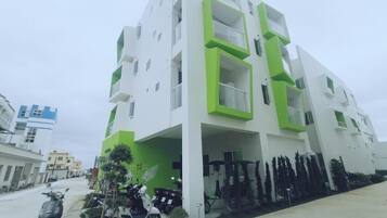 Un immeuble résidentiel moderne à plusieurs étages, doté de balcons, d’un espace de stationnement et d’une rangée d’arbres.