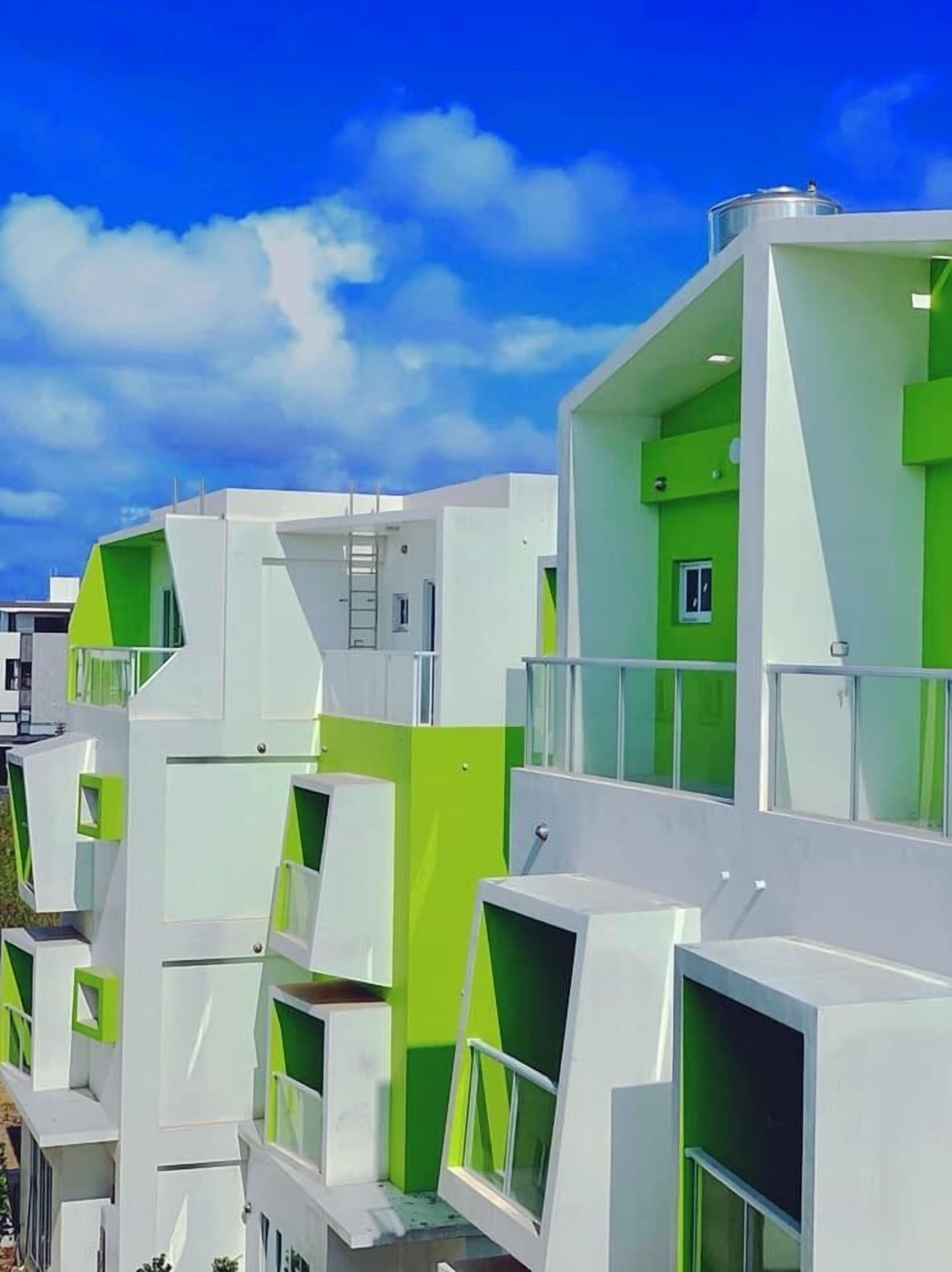 Ein modernes Gebäude mit mehreren Balkonen und großen Fenstern, das sich durch ein geometrisches Design in Weiß und Grün auszeichnet.