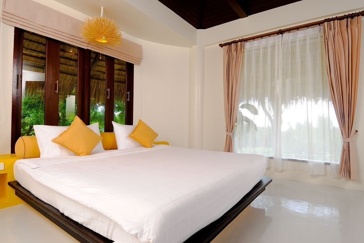 A bedroom with a bed, curtains, and a view of greenery.