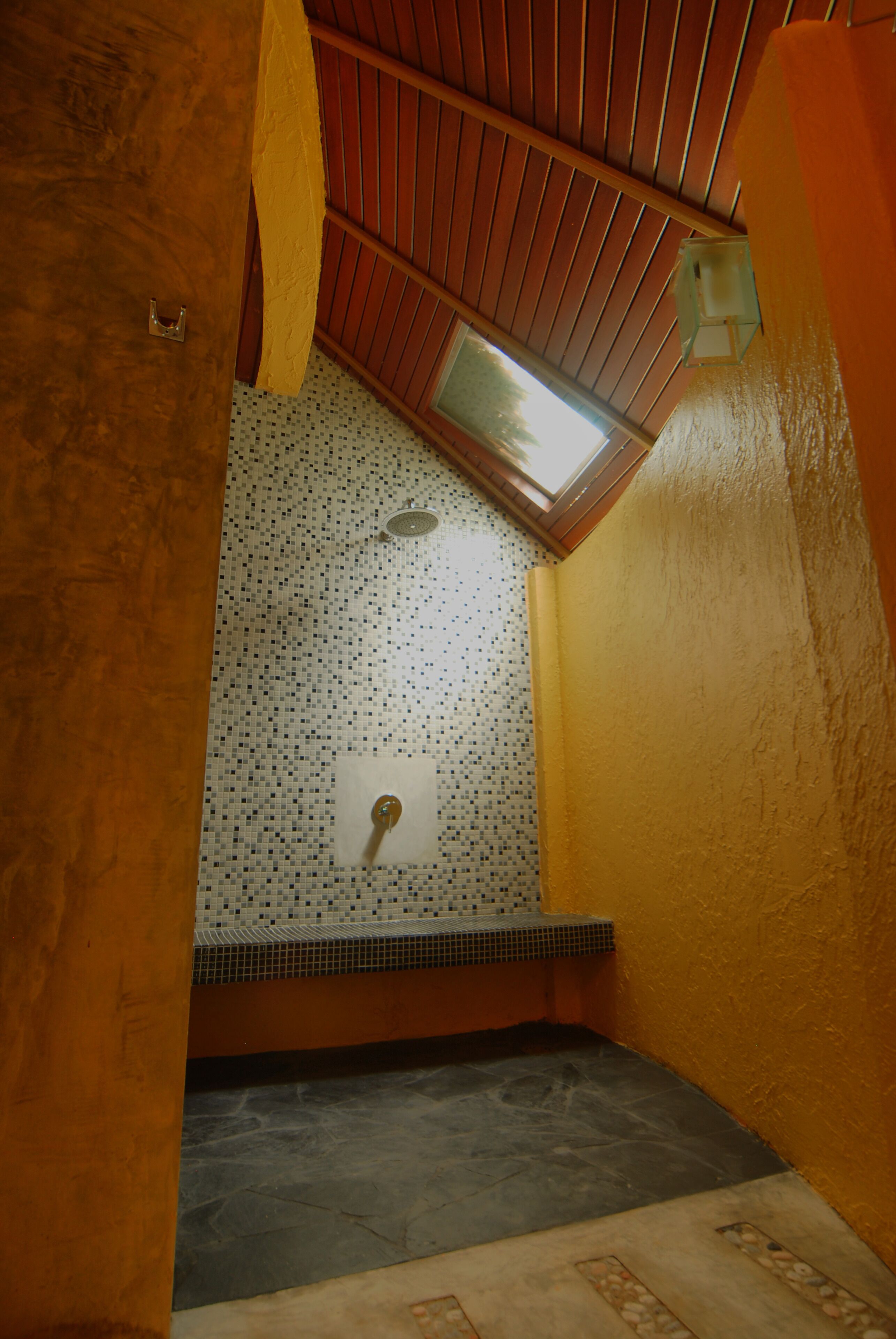 A bathroom with a tiled floor, a shower area, and a skylight.
