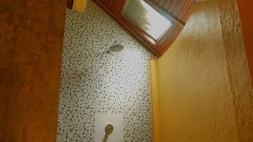 A bathroom with a tiled floor, a shower area, and a skylight.