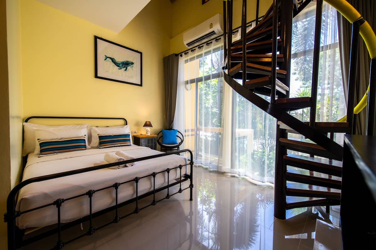 A bedroom with a bed, a nightstand, a chair, a staircase, and a window with curtains.