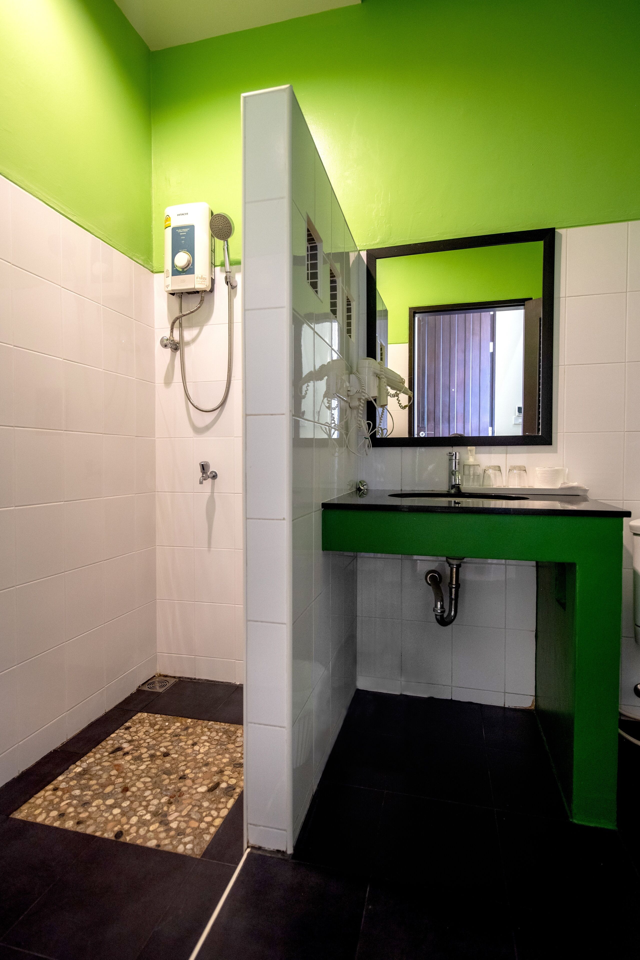 A bathroom with a green and white color scheme, a shower with a handheld showerhead, a sink with a mirror above it, and a tiled floor with a pebble pattern.
