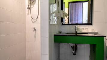 A bathroom with a green and white color scheme, a shower with a handheld showerhead, a sink with a mirror above it, and a tiled floor with a pebble pattern.