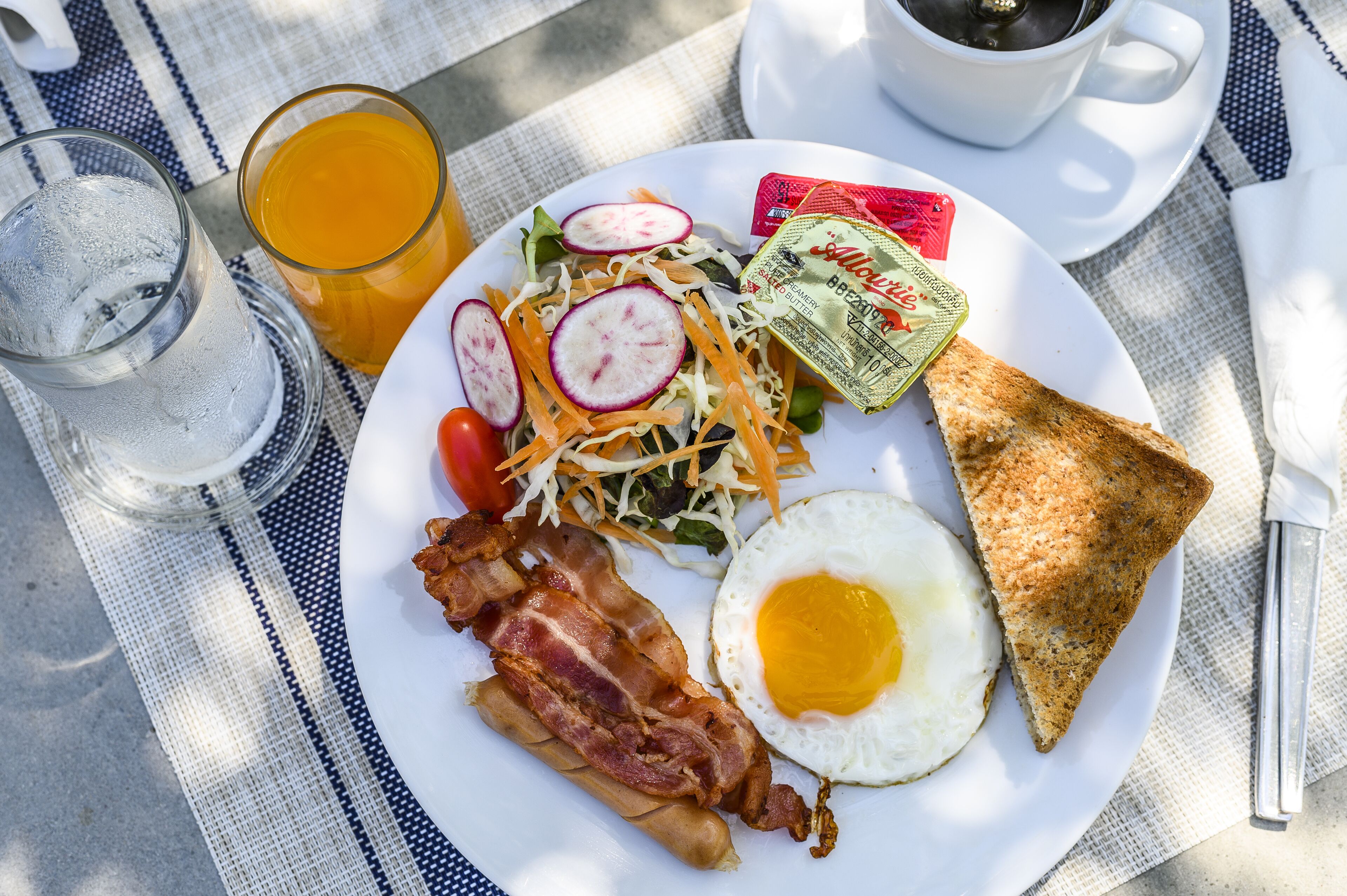 A breakfast plate with bacon, an egg, toast, a salad, and juice.