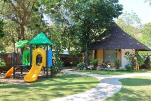 A playground with a slide and climbing structures, surrounded by a well-maintained lawn and a small gazebo.
