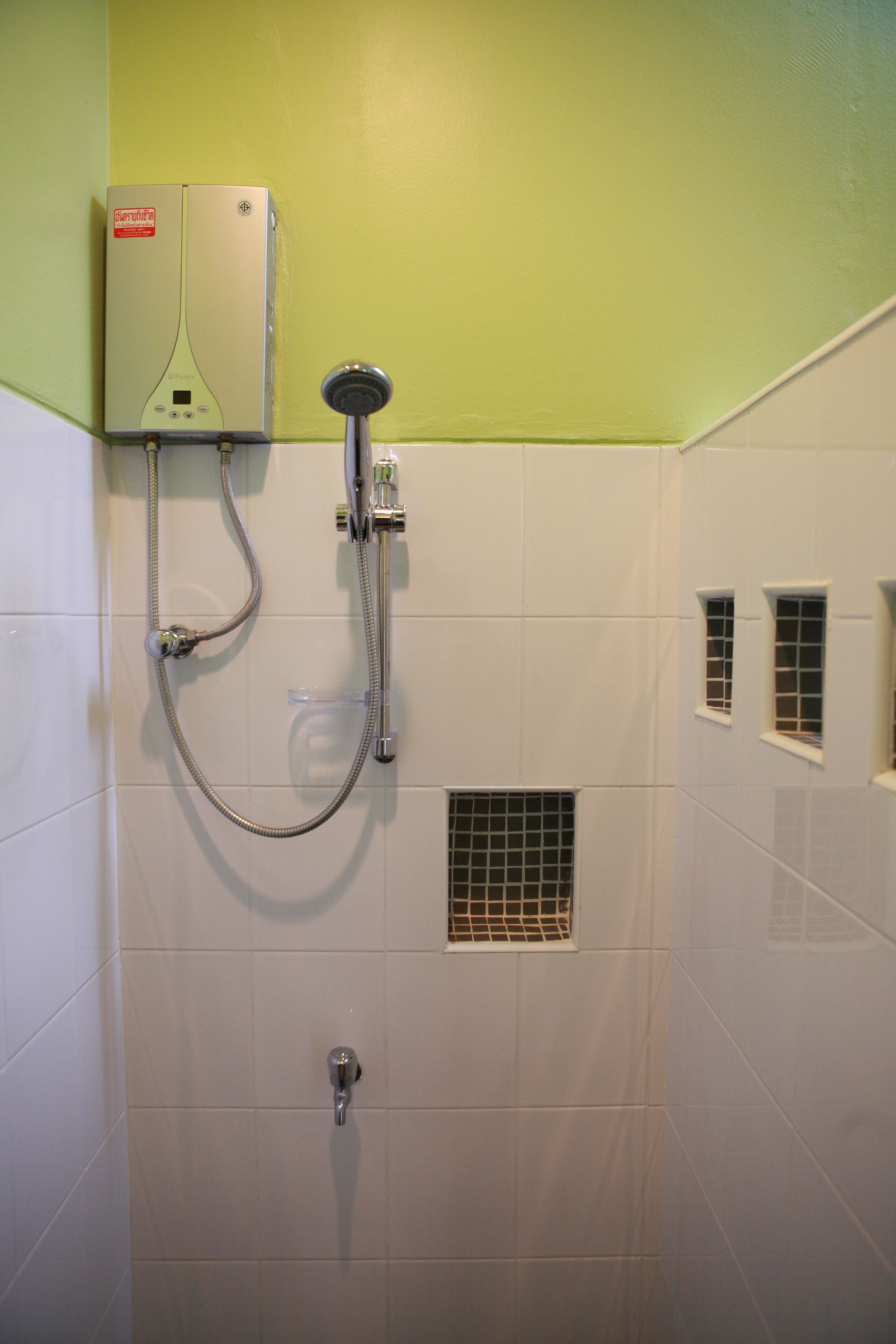 A bathroom with a built-in shower, a wall-mounted heater, and a small window.