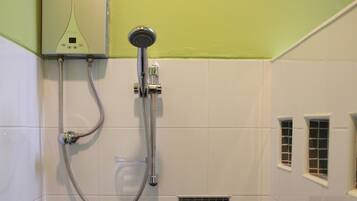 A bathroom with a built-in shower, a wall-mounted heater, and a small window.