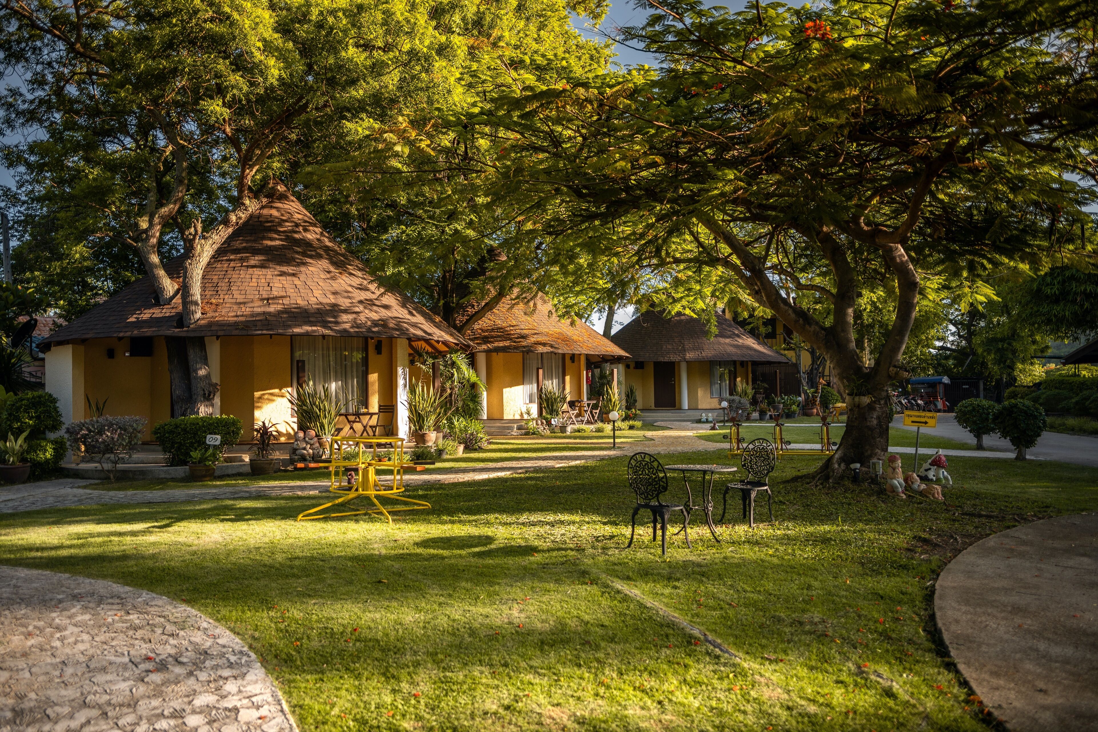 A bungalow-style hotel with thatched roofs, a well-maintained lawn, and outdoor seating areas.