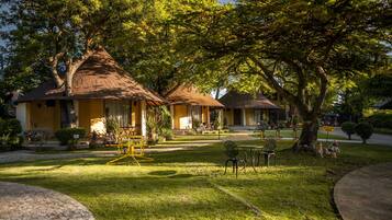 A bungalow-style hotel with thatched roofs, a well-maintained lawn, and outdoor seating areas.