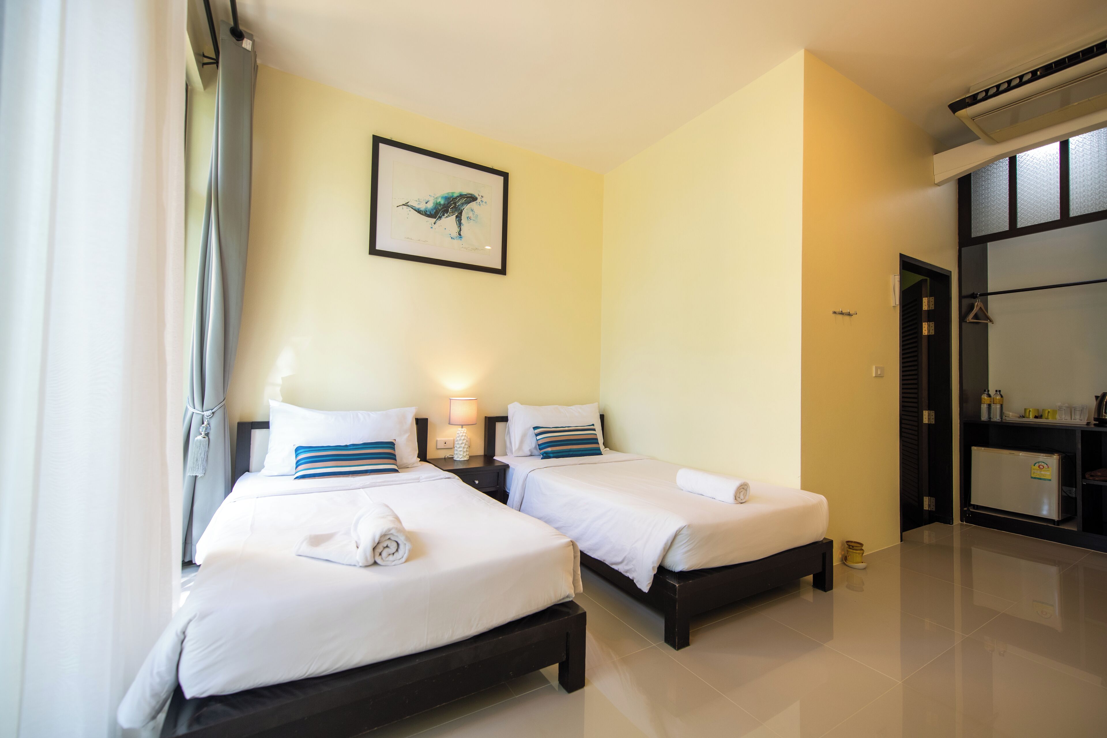 A hotel room with two beds, a framed artwork on the wall, and a small kitchenette.