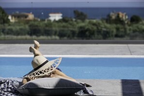 Eine Person entspannt am Pool mit Blick auf das Meer und Gebäude im Hintergrund.