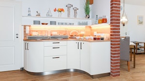 A modern kitchen with white cabinets, a curved countertop, and a brick column. - Double room - Double room in the Hotel-Pension Marlies (Neuharlingersiel)