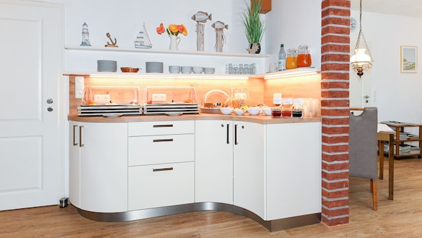 Una cocina moderna con armarios blancos, una encimera curva y un pilar de ladrillo.