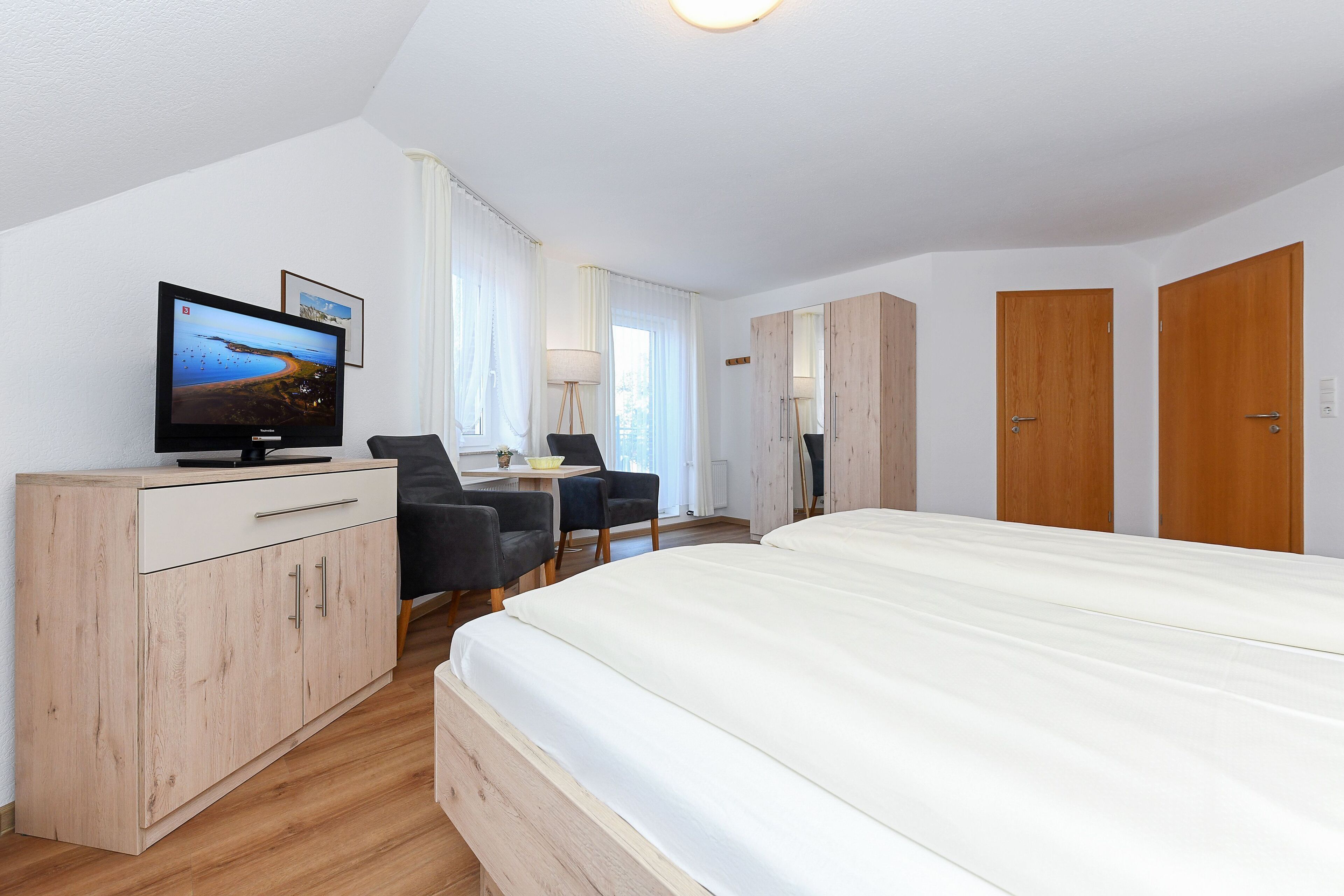 A bedroom with a bed, a desk, a chair, a TV, and wooden wardrobes.
