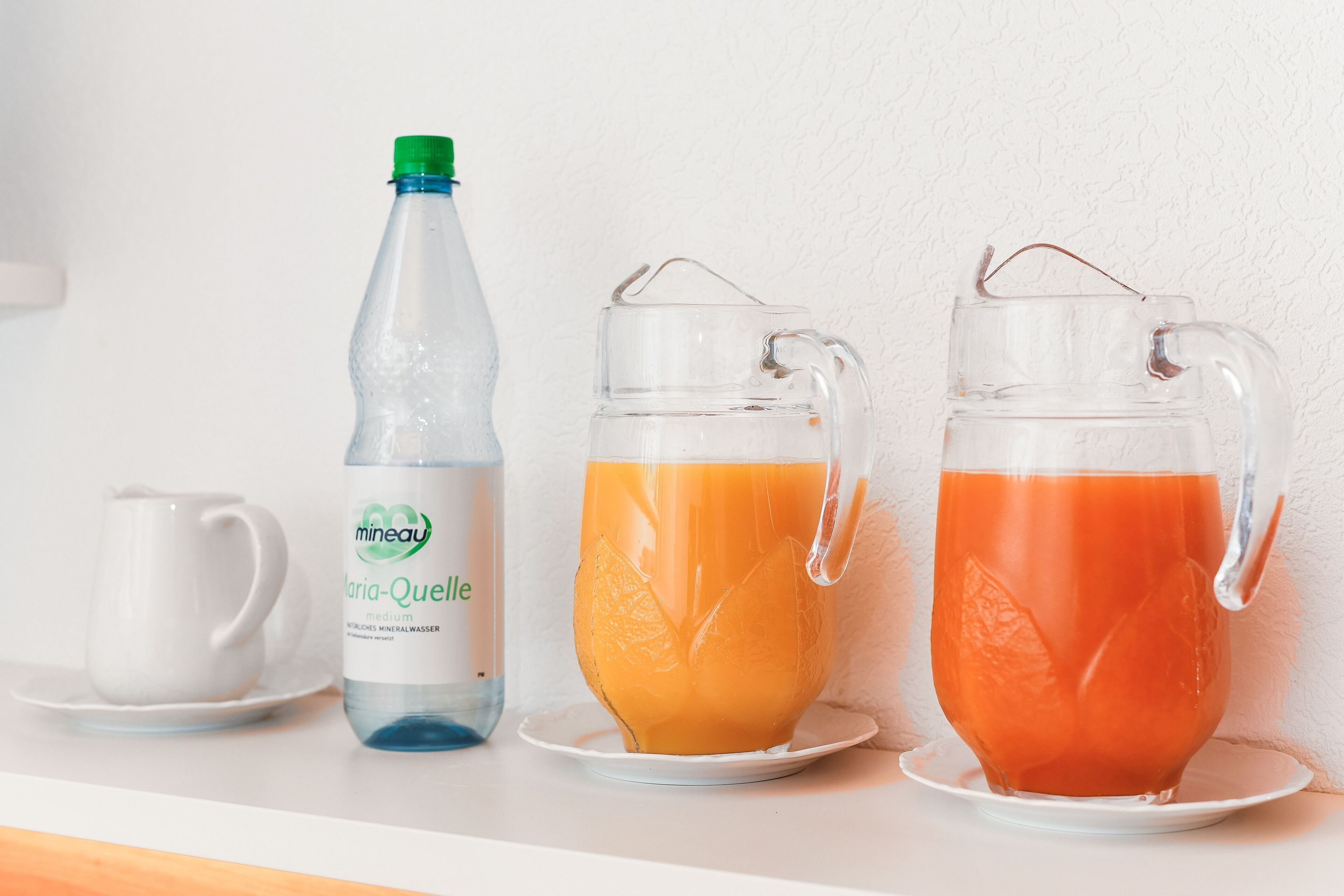 Une table où sont disposés une bouteille et deux carafes sur une surface blanche.