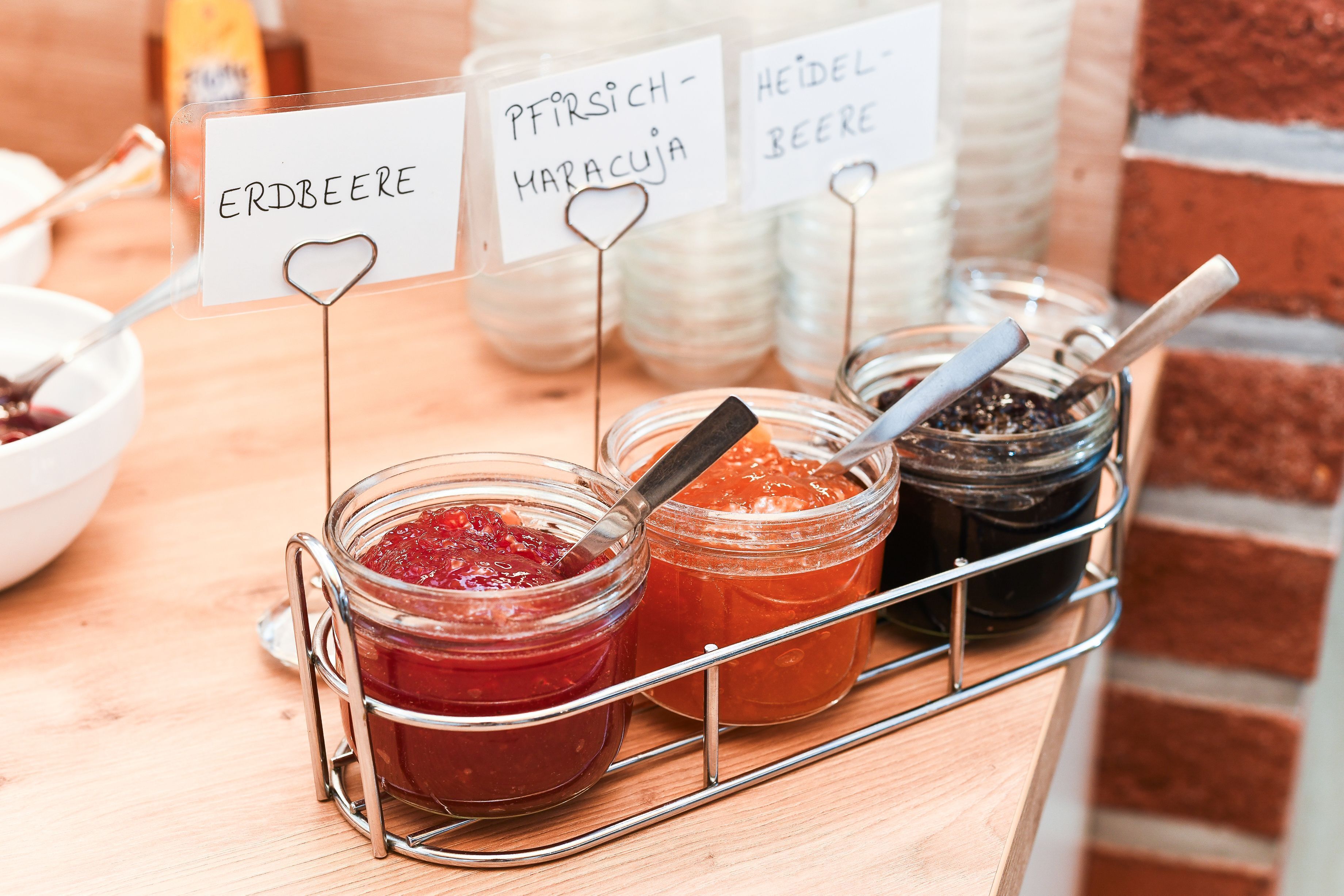 A selection of jars with labels indicating different types of spreads, such as Erdbere, Pfirsich-Maracuja, and Heidelbeere, arranged on a metal rack.