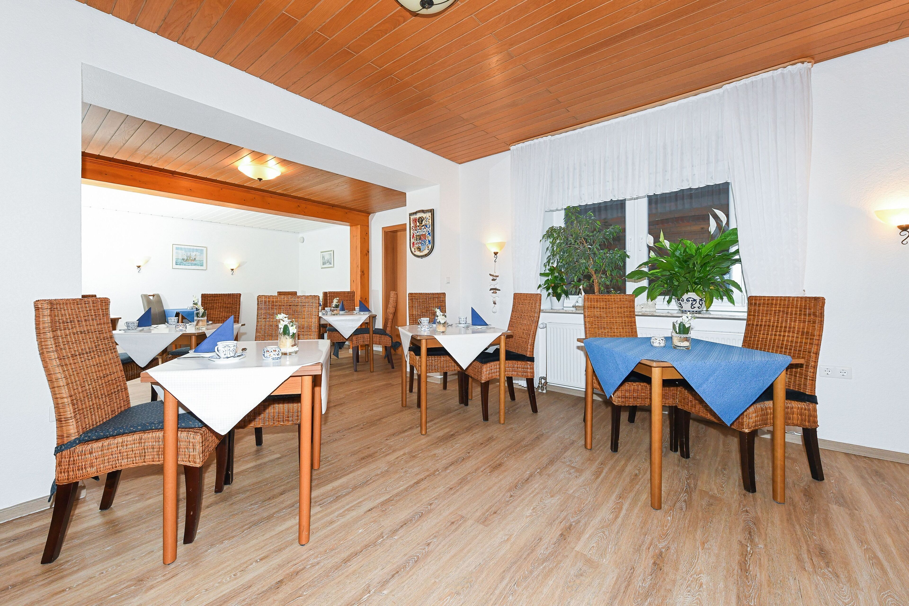 Un comedor con pisos de madera, sillas de mimbre y mesas cubiertas con manteles azules.