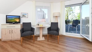 Ein modernes Zimmer mit Fernseher, zwei Sesseln, einem kleinen Tisch und Balkonblick.