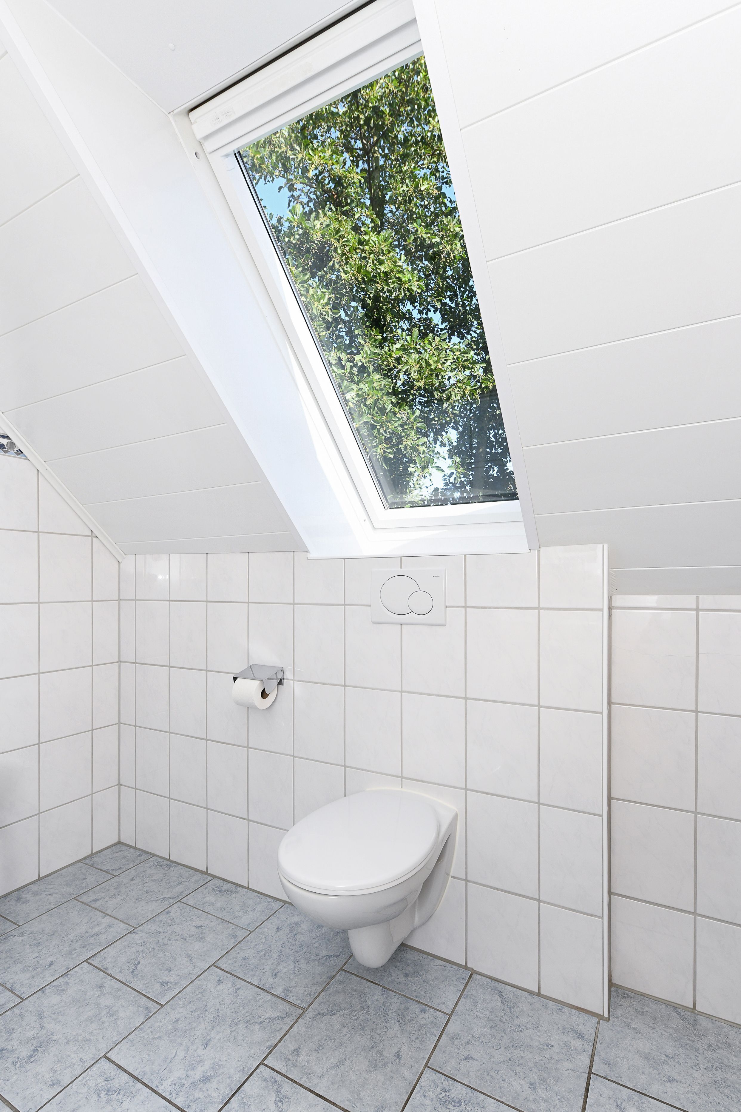 Un baño moderno con tragaluz, azulejos blancos y un inodoro.