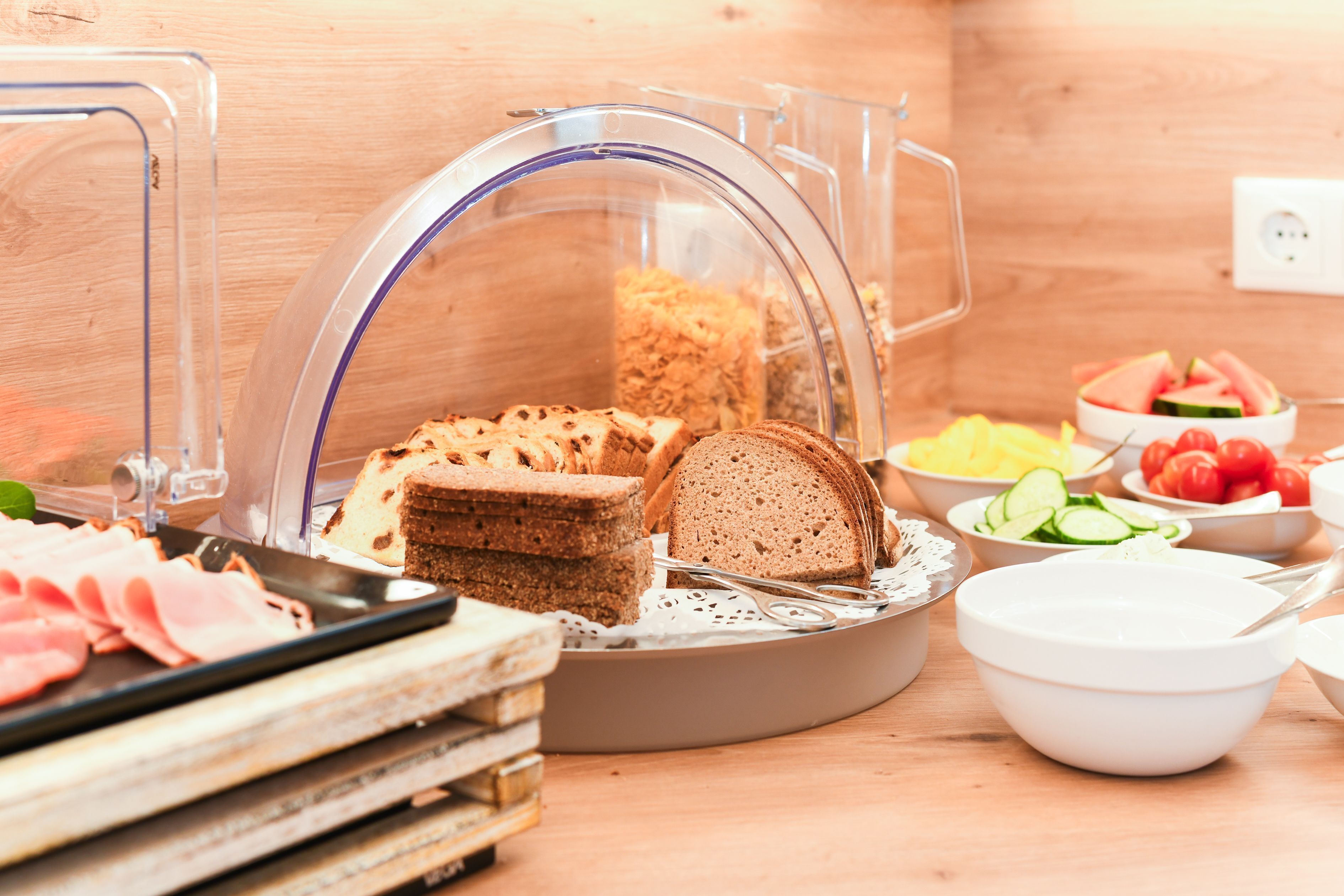 Ein reichhaltiges Buffet mit verschiedenen Speisen, darunter Brot, Schinken und frisches Gemüse.