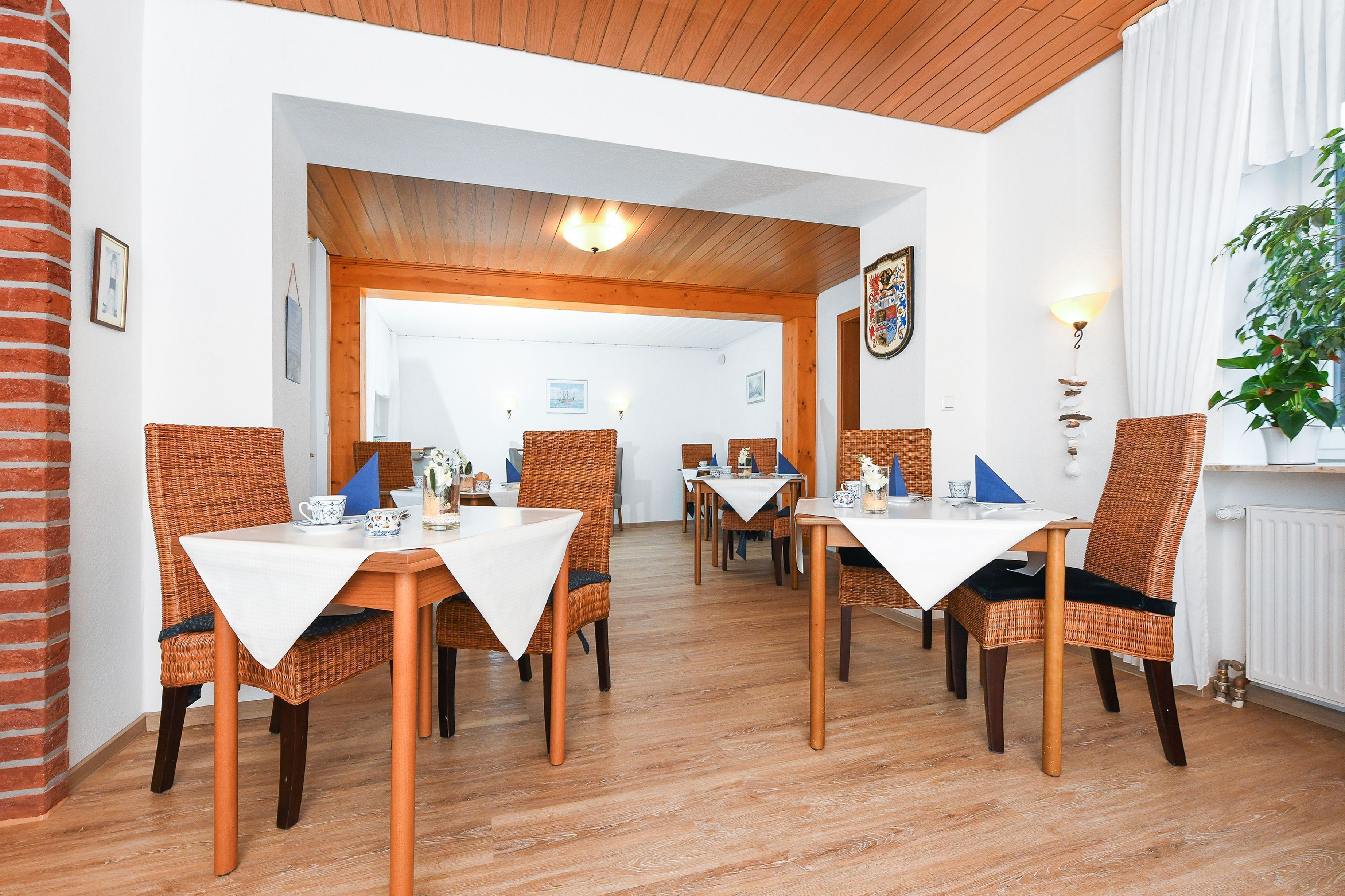 Un comedor con sillas de mimbre y manteles blancos, suelo de madera y pared de ladrillo.