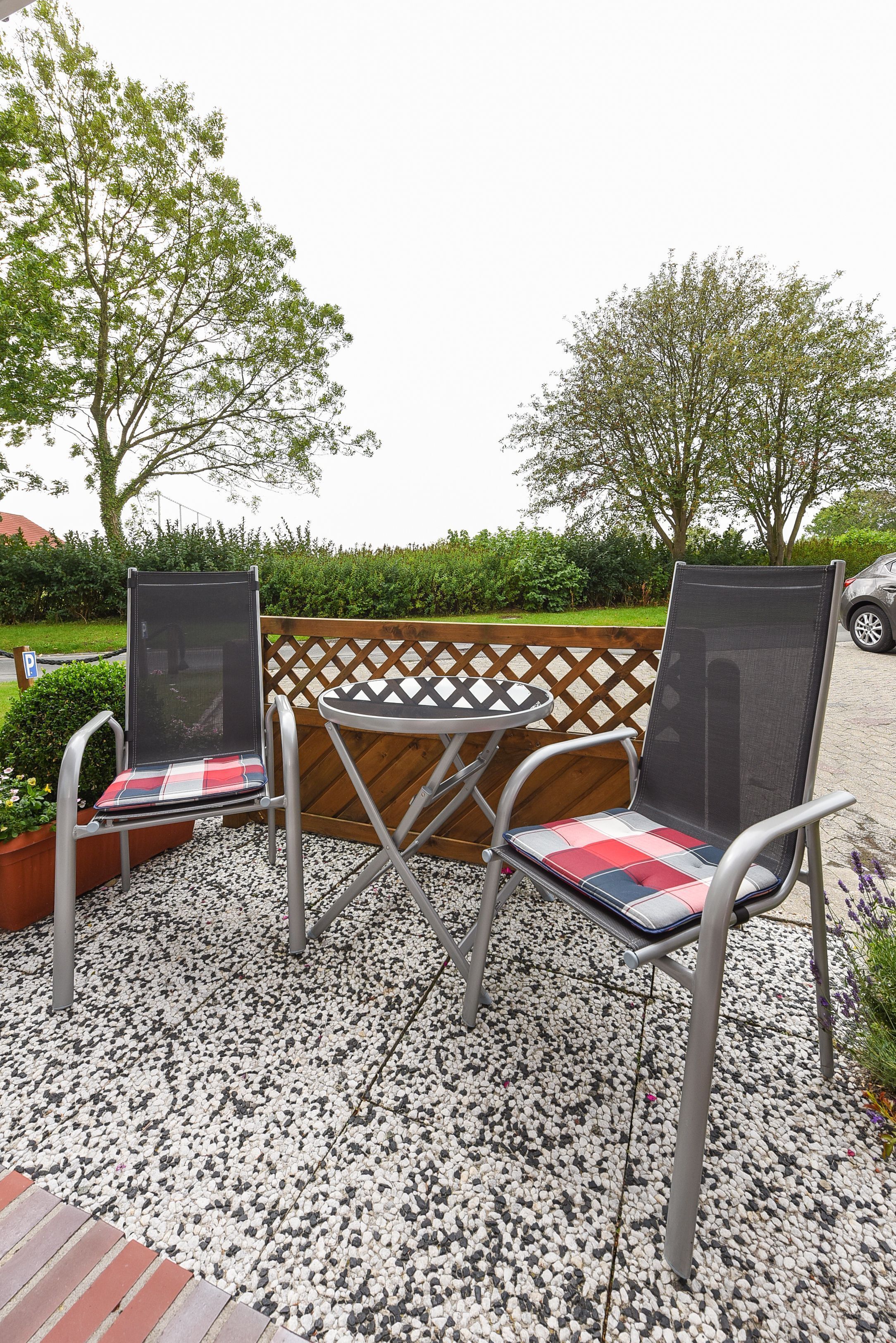 Two outdoor patio chairs with mesh backs and cushioned seats, placed on a gravel surface with a wooden fence and greenery in the background.