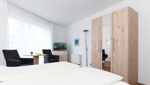 A hotel room with a large bed, a desk with a chair, a TV, and a wardrobe.