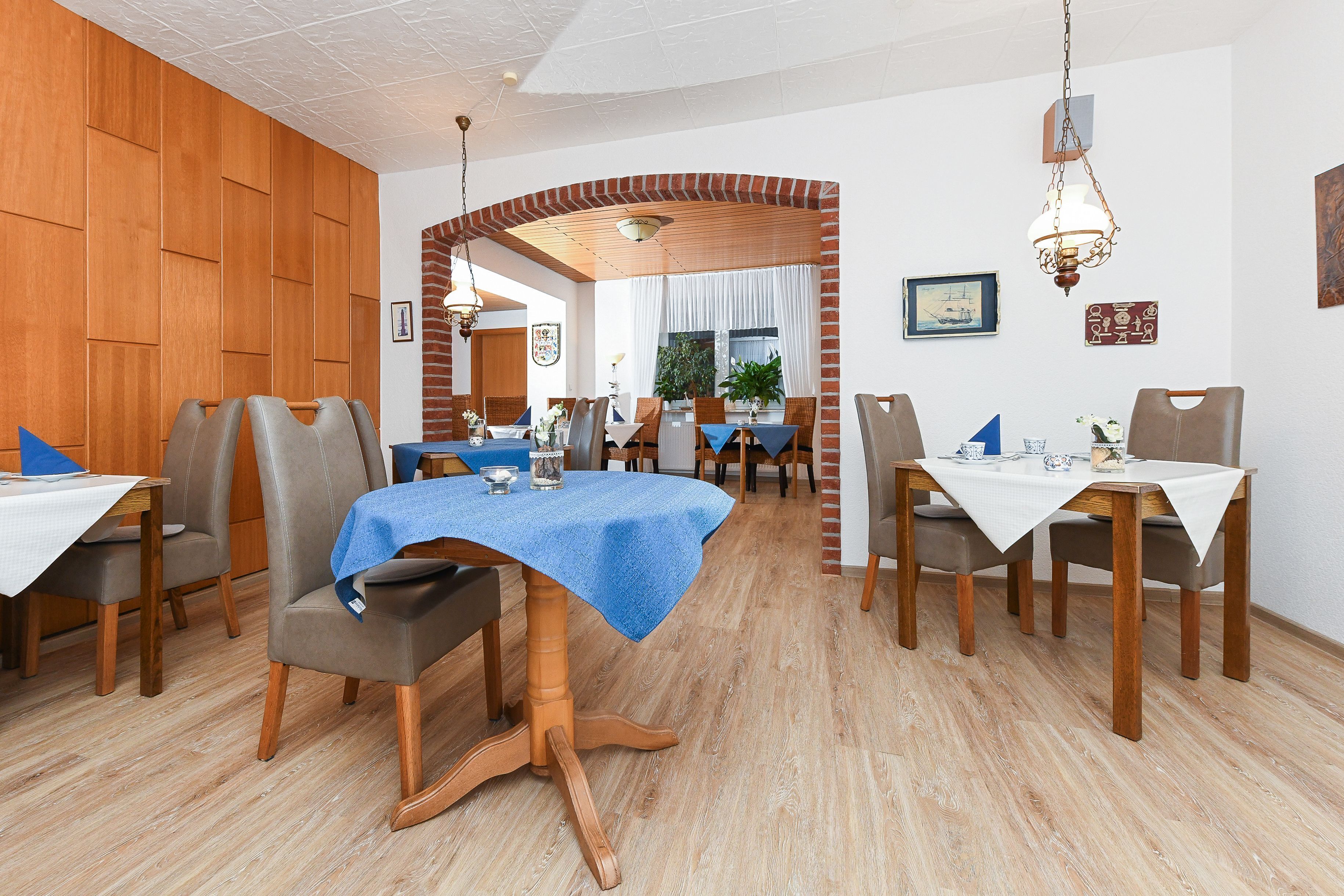 Comedor con paneles de madera, un arco de ladrillo y mesas con manteles azules.