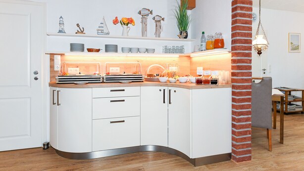 A modern kitchen with white cabinets, a curved countertop, and a brick column.