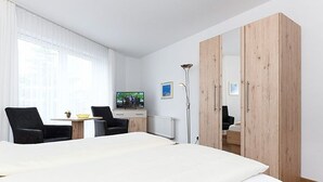 A hotel room with a large bed, two chairs, a desk, a TV, and a wardrobe.