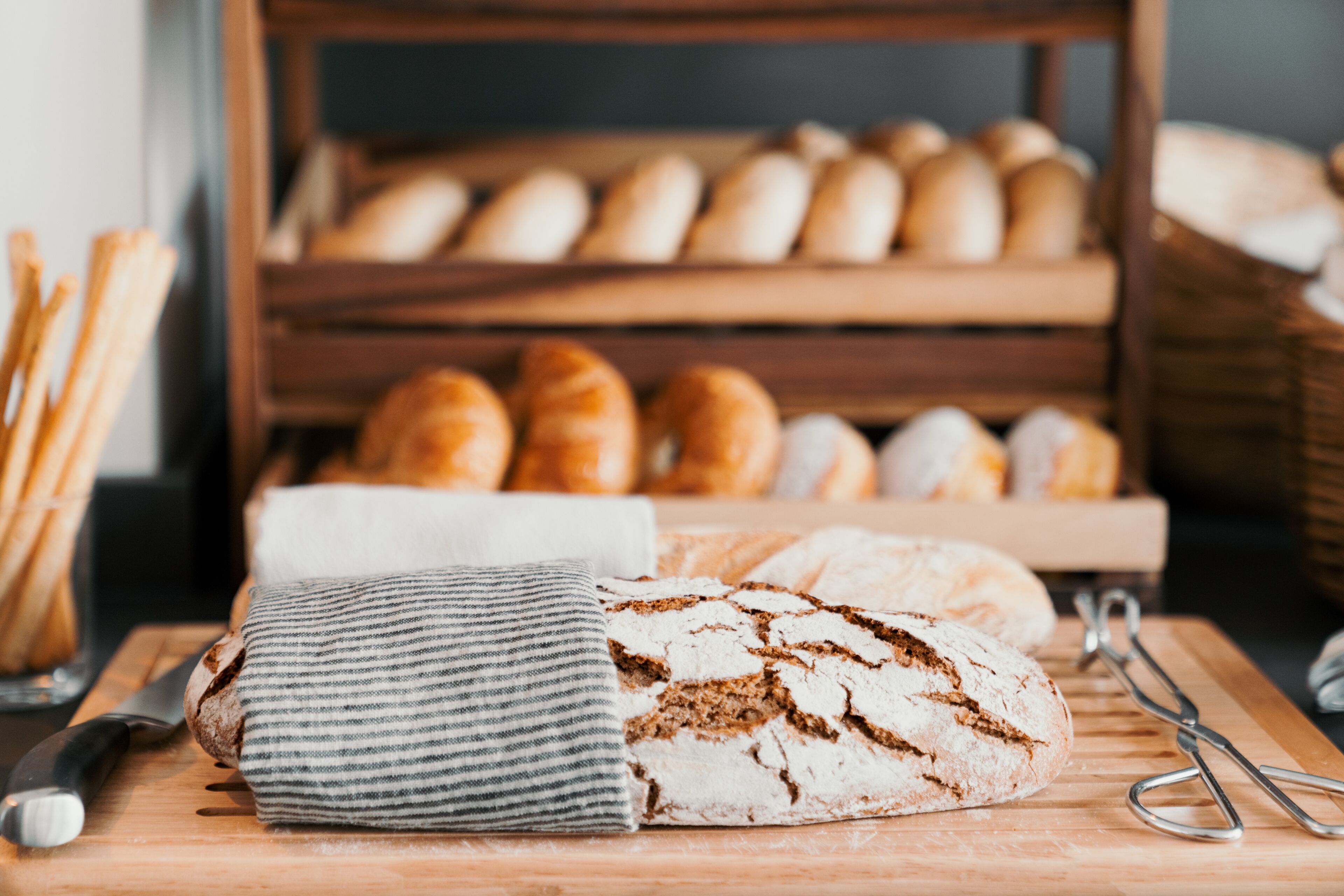 A wooden cutting board with a loaf of bread, a striped cloth, and a knife.