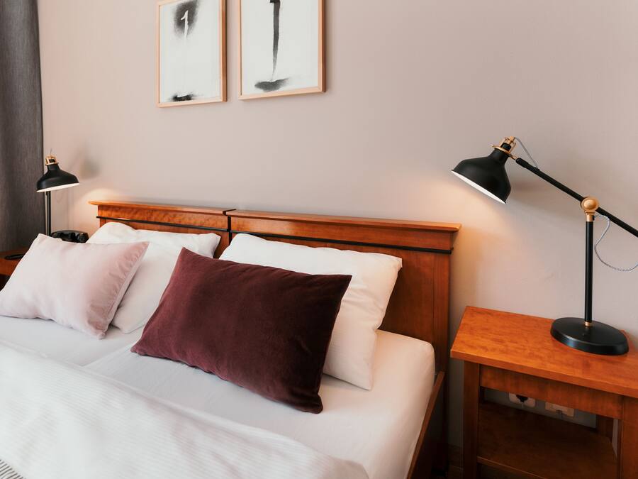 A neatly made bed with white and maroon pillows, a wooden headboard, and two bedside tables with lamps.