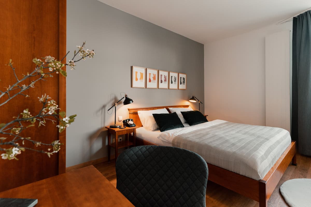 A hotel room with a bed, bedside tables, a chair, a desk, and a wall with framed pictures.