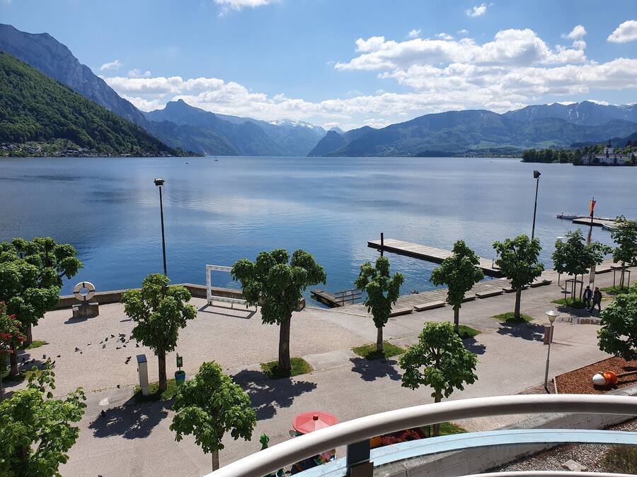 Paseo junto al lago con árboles, bancos y un muelle de madera.