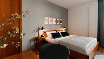 Habitación de hotel con cama, mesita de noche, lámpara, silla y pared decorada con cuadros.