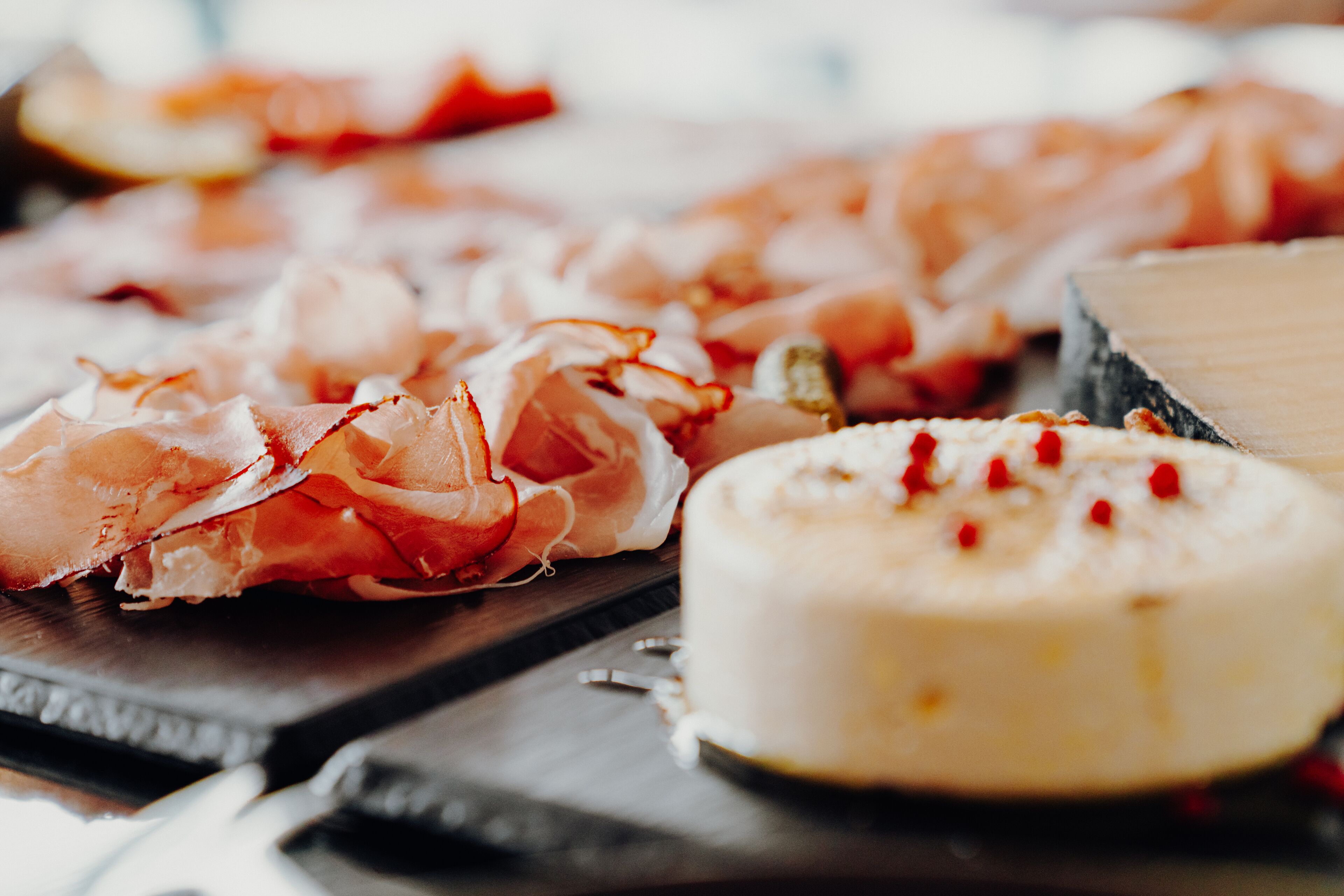 Diversos alimentos, como jamón serrano y un queso redondo, sobre una tabla de madera.