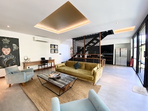 Relax in a stylish living space with a sofa, armchair, and coffee table, surrounded by artwork and a large window offering a view of the outdoors.