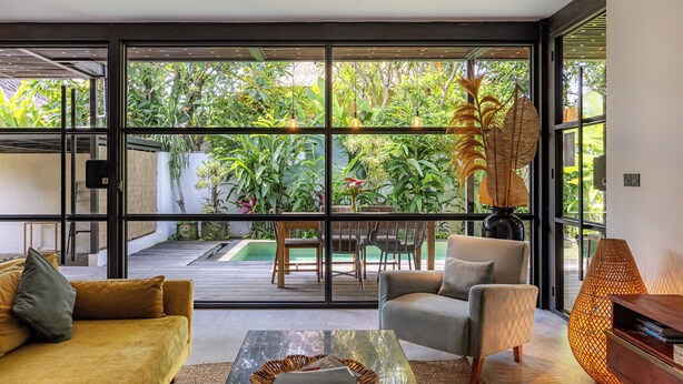 Un salon moderne doté de grandes portes vitrées donnant sur un jardin. On y trouve deux canapés, une table basse et une lampe.