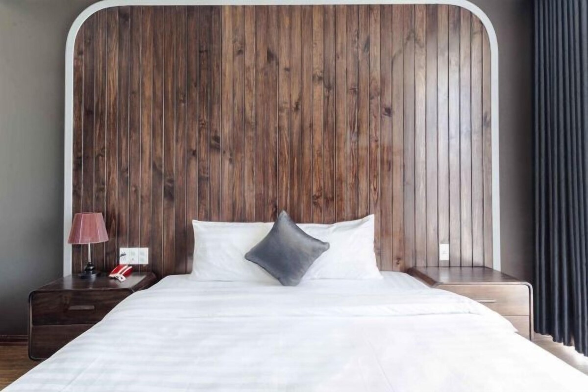 A hotel room with a wooden headboard, a bed with white linens, a nightstand with a lamp, and a telephone.