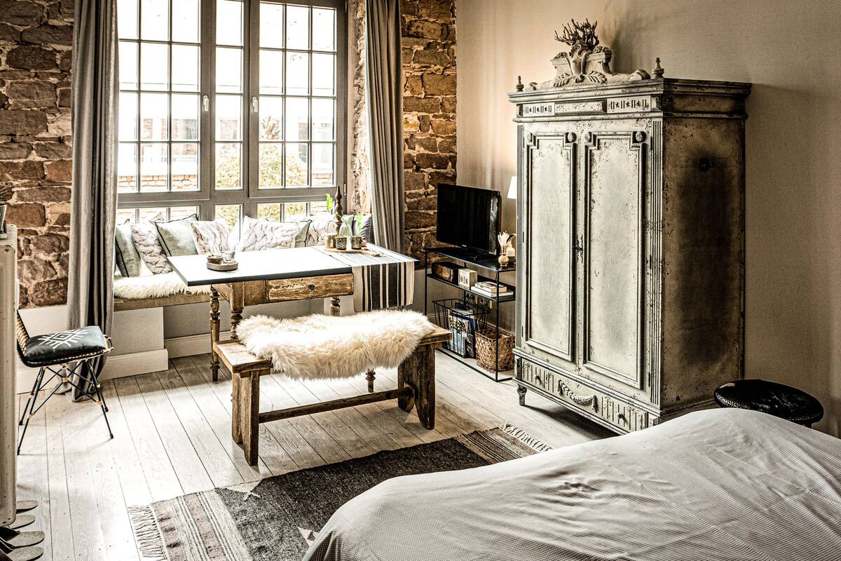 Une pièce chaleureuse avec un mur en pierre, un banc en bois, une table avec une lampe, un téléviseur posé sur une étagère et un lit.