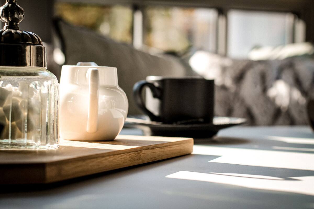 Une table en bois sur laquelle se trouvent un bocal en verre, une théière blanche et une tasse noire posée sur une soucoupe.