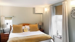 A neatly arranged bedroom with a bed, bedside tables, a nightstand, a window with curtains, and a wall-mounted cabinet.