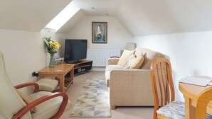 A cozy loft-style living room with a sloped ceiling, a television, a sofa, a wooden coffee table, and a chair.