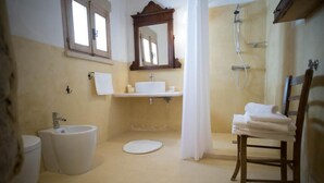 Une salle de bain équipée de toilettes, d’un bidet, d’un lavabo, d’un miroir, d’une douche et d’une chaise avec des serviettes.