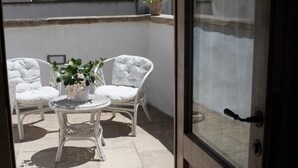 An outdoor seating area with two white wicker chairs and a small round table, a potted plant, and a view through a glass door. - Dimora Storica   Nonna Adelina (Corigliano D'otranto)