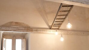 A room with exposed wooden beams, a ladder, and hanging light bulbs. - Dimora Storica   Nonna Adelina (Corigliano D'otranto)